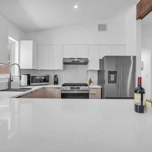 Fully equipped modern kitchen featuring sleek white cabinetry, stainless steel appliances, and a spacious island with bar seating