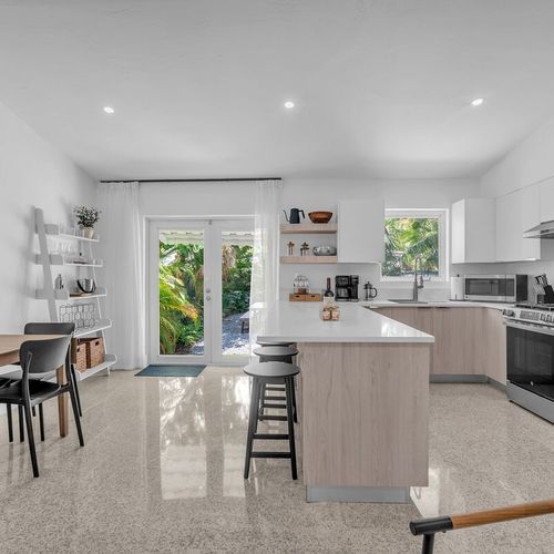 Fully equipped modern kitchen featuring sleek white cabinetry, stainless steel appliances, and a spacious island with bar seating