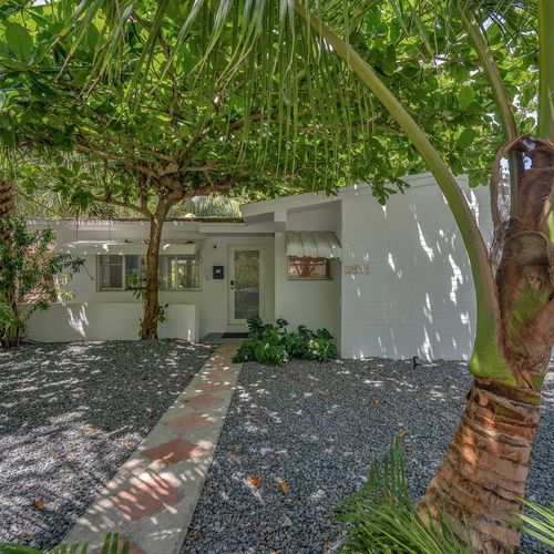 A warm welcome to your private stay—walk along the paved pathway shaded by lush tropical trees and palms leading to the crisp, white entrance.