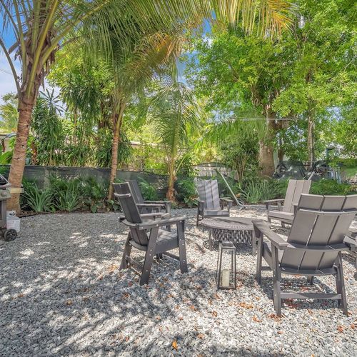 Private backyard retreat featuring a firepit with seating, picnic-style dining table, and a grill for al fresco cooking under the palms.