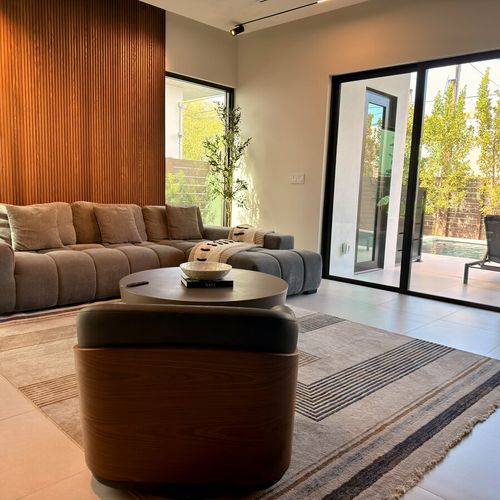 The room highlights an elegant neutral color palette, premium area rugs, and floor-to-ceiling windows that fill the modern interior with abundant natural light.