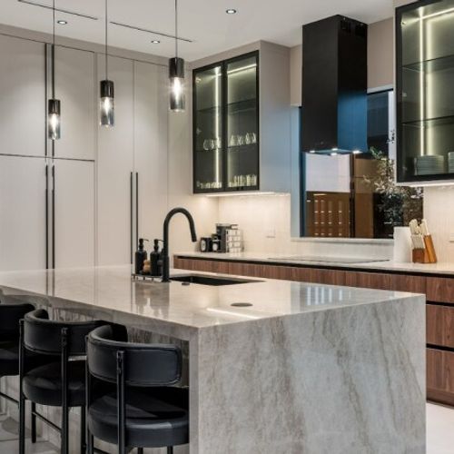 The layout highlights a functional yet stylish design with black leather bar stools, professional-grade matte black fixtures, and glass-front upper cabinets with integrated LED accent lighting.