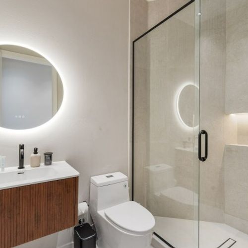 Step into a bright, refreshing oasis. This guest bathroom offers a luxurious, spa-like feel with its modern walk-in glass shower, premium rain showerhead, and a stylish wood-paneled vanity.