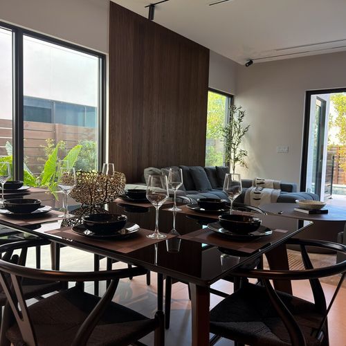 Perfectly set for entertaining, this room showcases a sleek dark wood dining set, premium glassware, and a warm, inviting atmosphere created by the architectural wood accents and minimalist design.
