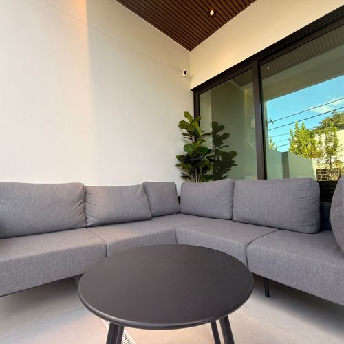 Relax in style in this sophisticated outdoor lounge. Featuring a plush, contemporary sectional sofa and a sleek coffee table, this covered patio area offers the perfect spot for morning coffee or evening relaxation.