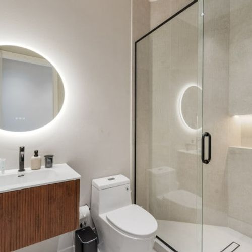 Step into a bright, refreshing oasis. This guest bathroom offers a luxurious, spa-like feel with its modern walk-in glass shower, premium rain showerhead, and a stylish wood-paneled vanity.