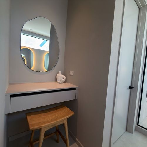 Elevate your morning routine in this chic, modern vanity nook. Featuring a sleek floating desk, an organic-shaped mirror, and premium finishes, this dedicated prep space is designed for ultimate comfort and style.