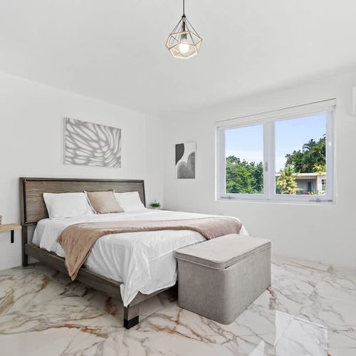 Modern master bedroom with king sized bed, with modern and soft bedding,  storage space, airconditioner, modern natural plants, warm lighting and bed tables. natural light and big windows. showcases wall art over the bed.