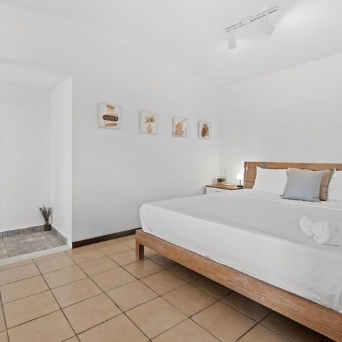 A modern and minimalist bedroom featuring a bed, tiled flooring, and a gallery wall of abstract artwork.