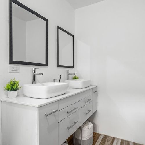 A well-lit bathroom featuring a rain shower, large mirror, modern double  vanity, white comfortable toilet., storage cabinets, modern finishings