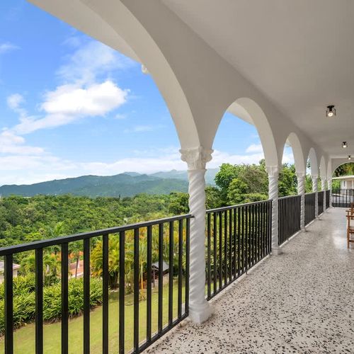 A long arched balcony offering stunning panoramic views of lush green mountains and a clear blue sky.