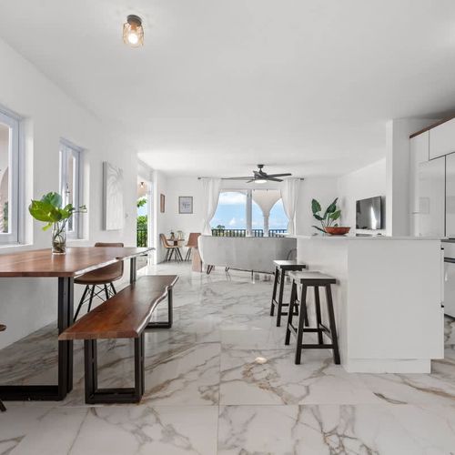 A spacious wooden dining table with access to the balcony with views, with marble flooring,, natural plants. lots of natural light and incredible views. white  kitchen with large countertop for big families. microwave, double door fridge with freezer