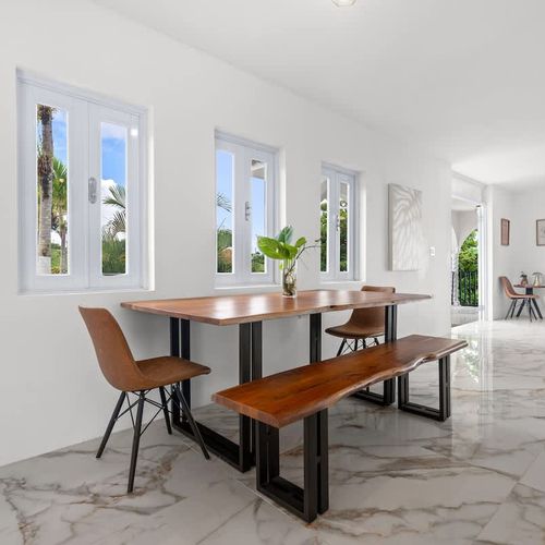 A bright airy dining room with large windows offering stunning outdoor views features a large wooden table.