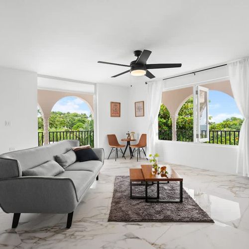 A spacious and modern open-plan living area with access to the balcony with views, with marble flooring, smart tv, ceiling fan, natural plants, coffee table and cozy grey sofa. lots of natural light and incredible views