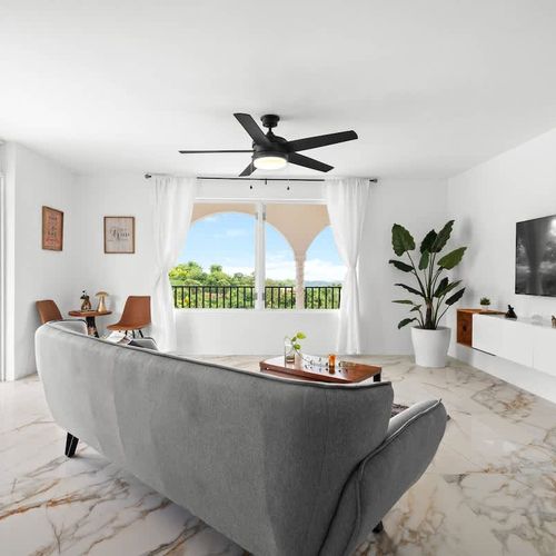 A spacious and modern open-plan living area with access to the balcony with views, with marble flooring, smart tv, ceiling fan, natural plants, coffee table and cozy grey sofa. lots of natural light and incredible views