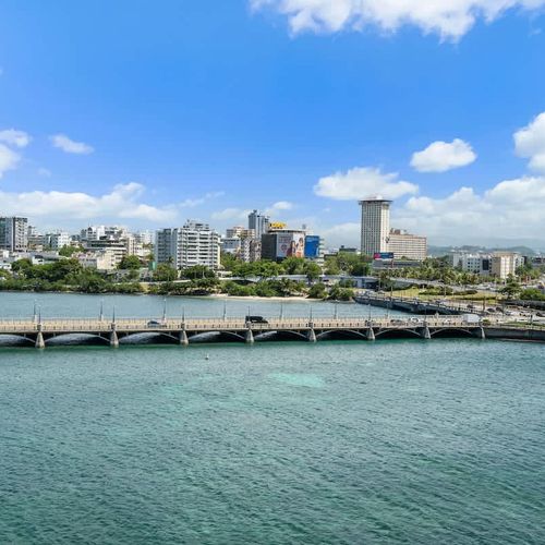 Enjoy the unique vantage point where city vibrancy meets coastal tranquility, all under a beautiful clear sky with fluffy white clouds.