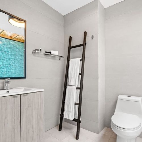This fresh and functional bathroom features a toilet, sink with a mirror, and a decorative ladder.