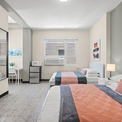 Discover comfort and space in this bright bedroom, featuring a plush bed and a full-length mirror, perfect for getting ready to explore the city or a last-minute check before heading out.