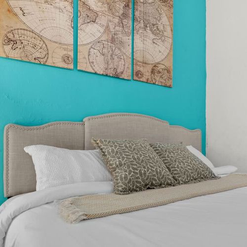 main bedroom with double bed, wall art, blue wall, large closet with mirror. bed side table with reading lamp and airconditioner. cushions and blankets