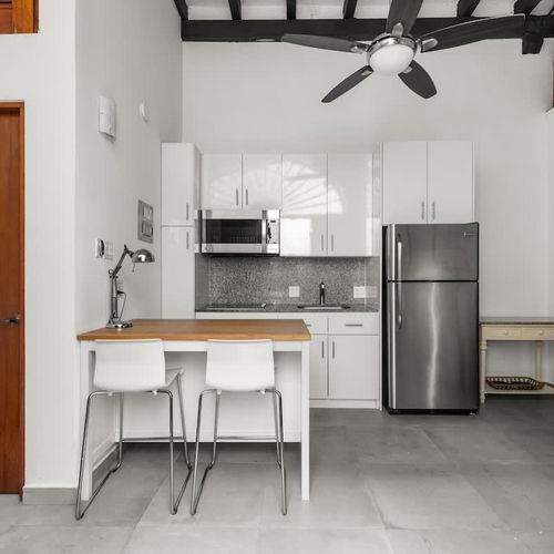 open kitchen with stainless steel fridge, air conditioner, livingroom with sofabed, seats, ceiling fan, microwave,  reading lamps, cabinets