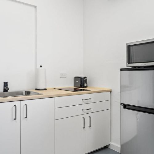 Delight in the practical elegance of this fully equipped kitchenette, featuring sleek stainless steel appliances, a warm wooden countertop, and crisp white cabinetry.