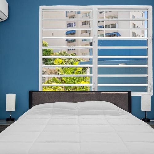 Experience tranquility in this stylish, modern bedroom with a striking blue accent wall and a cozy bed adorned with pristine white linens.