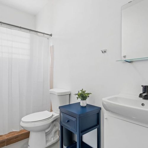 Relax in our serene white bathroom oasis, featuring a spacious mirror ideal for both your morning routine and evening unwind.