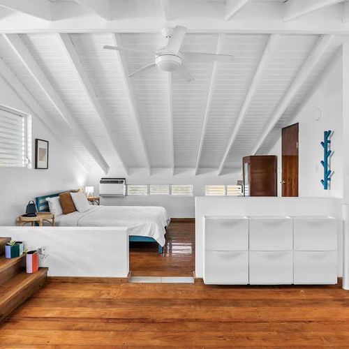 bedroom with bed and private balcony, air condiotioner, wall art and night table and drawers