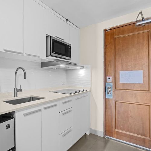Step into your bright and inviting studio apartment, featuring a modern kitchen equipped for all your culinary needs. Notice the handy fire extinguisher for peace of mind, ensuring a safe and comfortable stay.