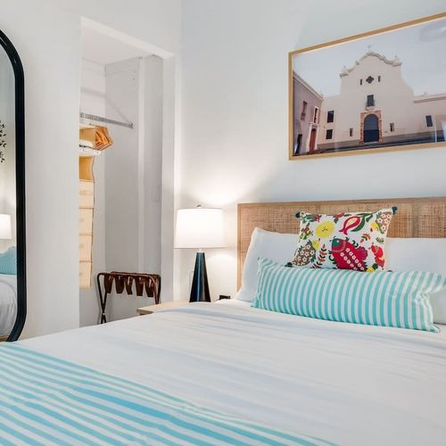 Cozy, modern bedroom, with wall painting and big mirror. nighlamps, and closet. Discover tranquility in this cozy, minimalist bedroom, thoughtfully crafted for comfort and serenity.