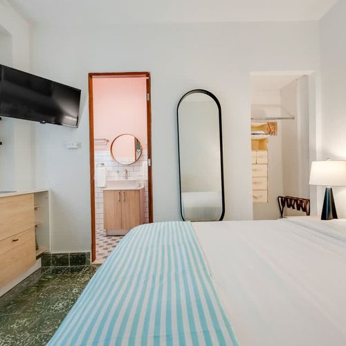 Relax and recharge in this serene minimalist bedroom bedroom, with wall painting and big mirror.  Has a provate bathroom, bedroom with drawers and closet. offering a cozy atmosphere, a stylish mirror, and a smart TV for your entertainment.