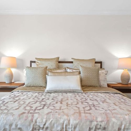 This  bedroom offers relaxation with its soft neutral tones and plush bedding. Textured pillows and a patterned comforter add tranquility, while stylish lamps and accents on the bedside tables enhance the inviting feel.
