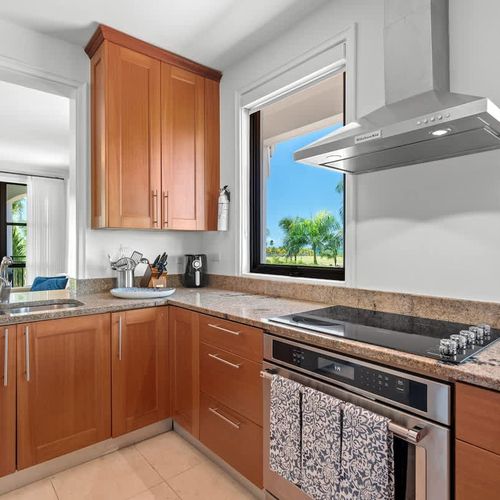 This kitchen combines modern and traditional design with stainless steel appliances, granite countertops, and warm wood cabinets. A large window offers stunning golf course views. It's well-equipped with a stovetop, oven, microwave, and fridge, and h