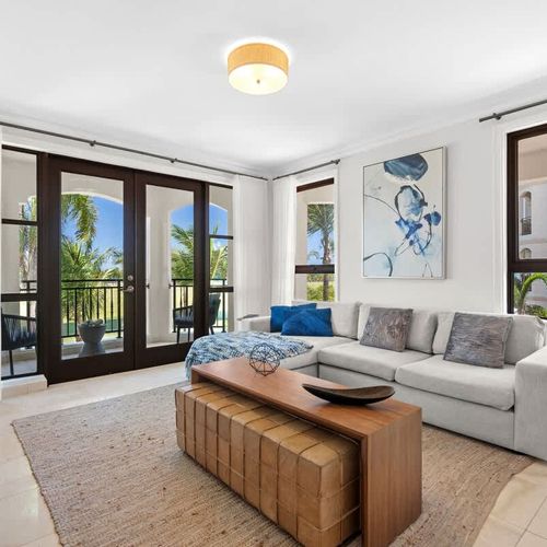 This inviting living space boasts a chic and modern design, with a comfortable L-shaped sofa, a stylish coffee table, and a large flat-screen TV. The room is bathed in natural light from the sliding glass doors that lead out to a spacious balcony, of