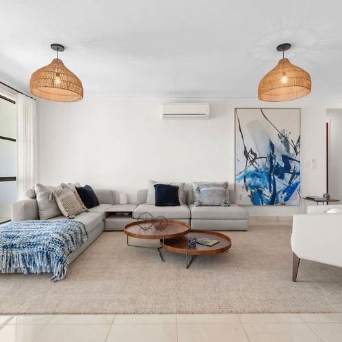 A modern living room with a comfortable sectional sofa, plush pillows, and a stylish coffee table. The room is bathed in natural light, creating a warm and inviting atmosphere. The artwork on the wall adds a touch of elegance, while the neutral color