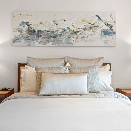 This serene bedroom invites relaxation with a plush bed, luxurious linens, and a neutral color palette. A captivating abstract artwork adds personality, while stylish bedside tables and lamps complete the tranquil ambiance.
