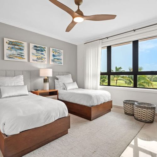 This serene and spacious guest bedroom is perfect for two. The twin beds, with their crisp linens and neutral colors, create a calming vibe. Large windows bring in lots of natural light and offer stunning views of the lush golf course. A ceiling fan
