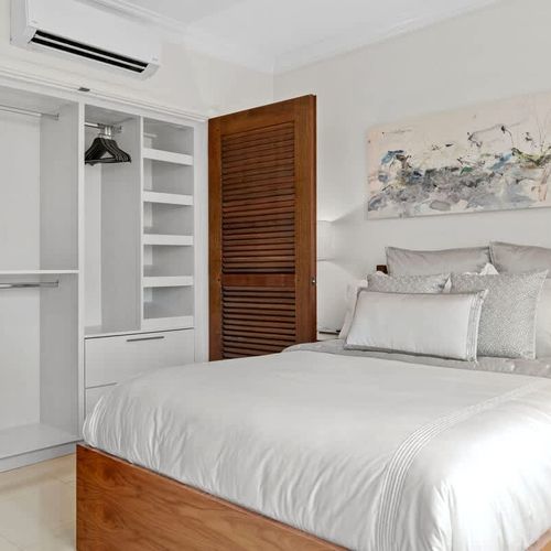 This serene bedroom blends modern elegance with comfort. The plush bed, white linens, and neutral colors create a relaxing vibe.