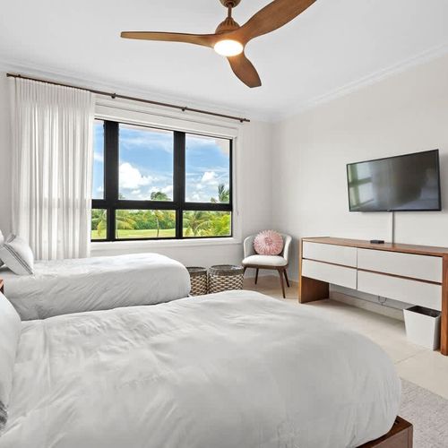 This bright and airy guest bedroom offers a tranquil retreat for two. The room features two twin beds dressed in crisp white linens and a neutral color palette, creating a calming atmosphere.