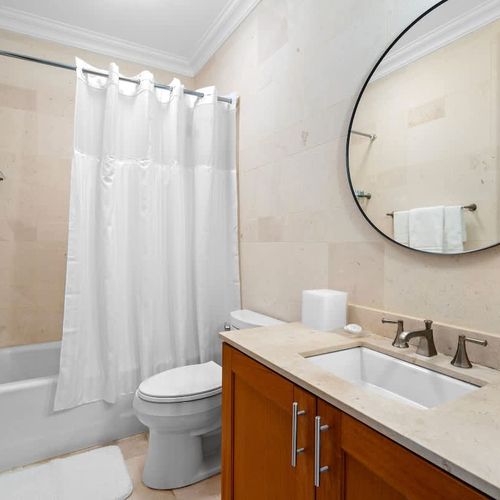 This bathroom is serene and inviting with neutral colors and modern fixtures. It features a spacious bathtub, a separate shower, a large vanity with ample counter space, and a round mirror for elegance. Plush towels and a bath mat add a touch of luxu
