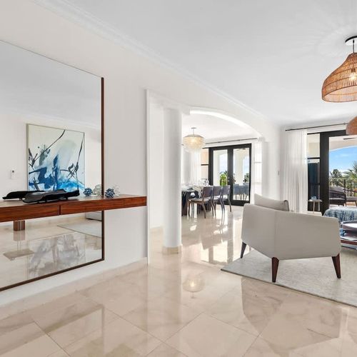 This expansive living room is a haven of relaxation and style. The plush seating arrangement, including a comfortable sofa and inviting armchairs, invites you to unwind and entertain in style. The sleek marble flooring and neutral color palette creat