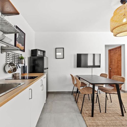 Enjoy a seamless experience of cooking, dining, and relaxing in this spacious kitchen area, featuring sleek appliances, a cozy dining table, and a flat-screen TV.