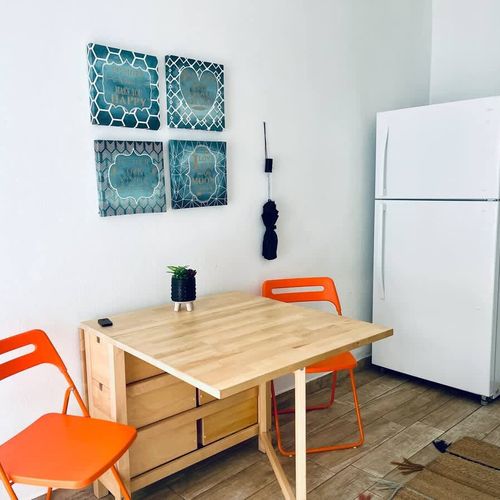 Savor your meals in our charming kitchen area, featuring a convenient fridge, a stylish dining table, and tasteful wall art to enhance your culinary experience.