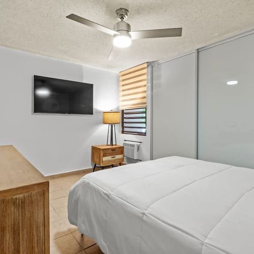 This modern bedroom is designed for relaxation, featuring a large bed with plush pillows and a convenient, sleek media setup for entertainment.