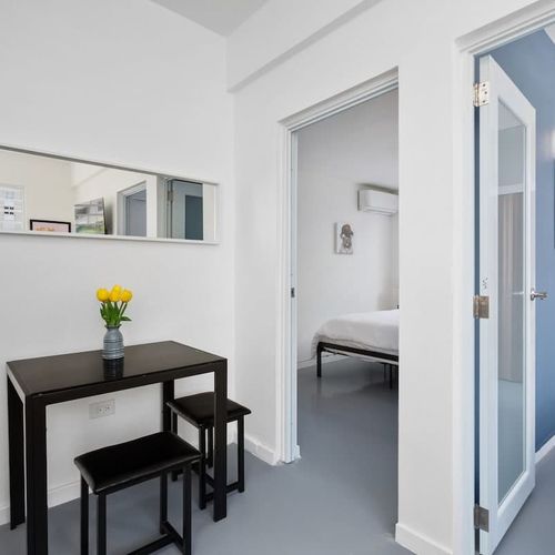 A black table is prominent at the forefront, holding a vase with yellow tulips. Above the table on the wall is a rectangular mirror reflecting part of the room.