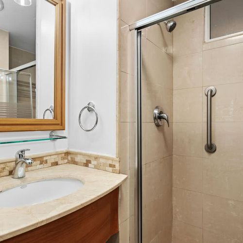 Our bathroom offers a refined experience with a beautiful wooden-framed mirror and a spacious vanity. The bright lighting ensures you have everything you need for your daily routine in a comfortable setting.
