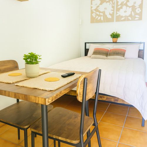 Bright and cozy studio setup with a comfortable full-size bed, wooden dining table for two, and soft neutral decor. Perfect for couples or solo travelers at Luna Suite, Casa Natura.