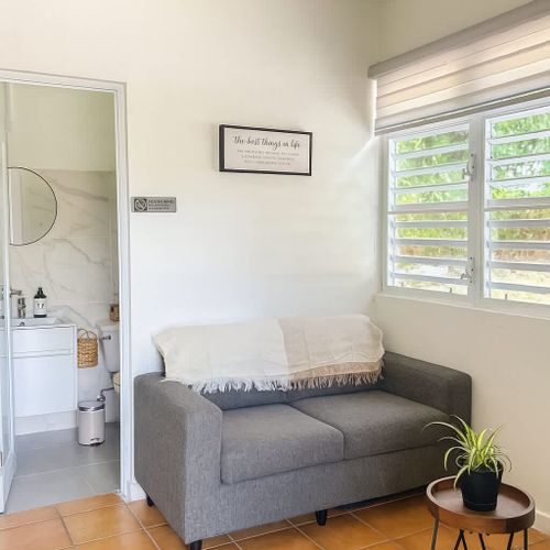 Bright and cozy lounge area with a modern sofa, natural light, indoor plant, and direct access to a clean, stylish bathroom. Perfect for relaxing after the beach at Luna Suite, Casa Natura.