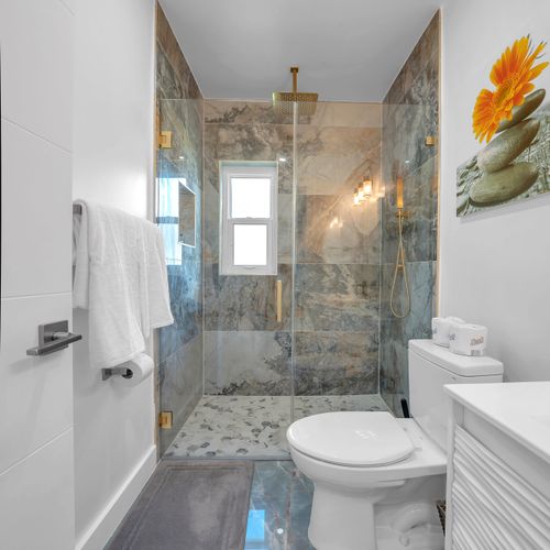 The recently upgraded bathroom is well-lit, thoughtfully stocck with the essential amenities, and adorned with beautiful marble tiles and a delightful rain shower.