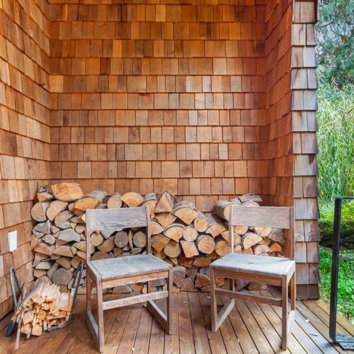 Perfectly stacked firewood and chairs for a welcoming fireplace experience.